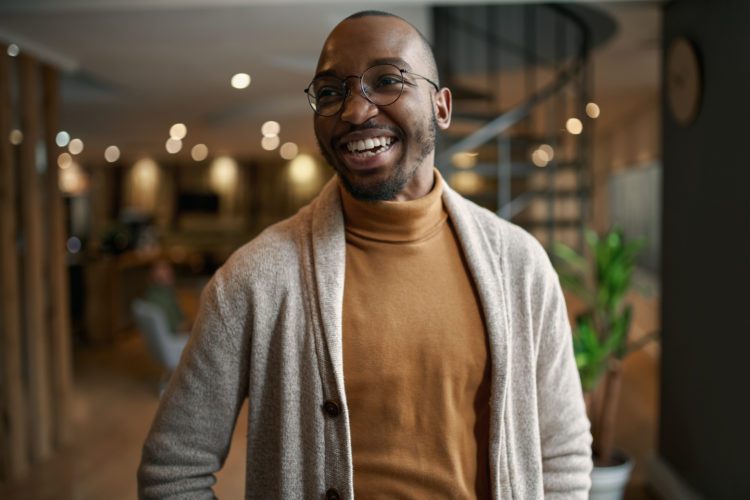 Happy portrait of Black entrepreneur laughing and smiling. feeling excited and positive. Wearing trendy clothing and eye glasses in a modern space